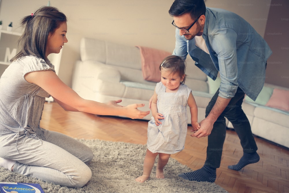 Family playing at home with their little baby. Parents together teaching their baby to walk."n