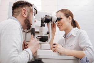 Bonne vue. Joyeuse professionnelle enchantée ophtalmologiste assise en face de son patient et scannant son œil tout en étant de bonne humeur