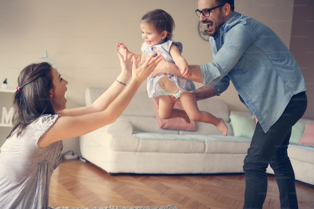 Familia jugando en casa con su pequeño bebé. Padre sosteniendo a la niña en las manos.