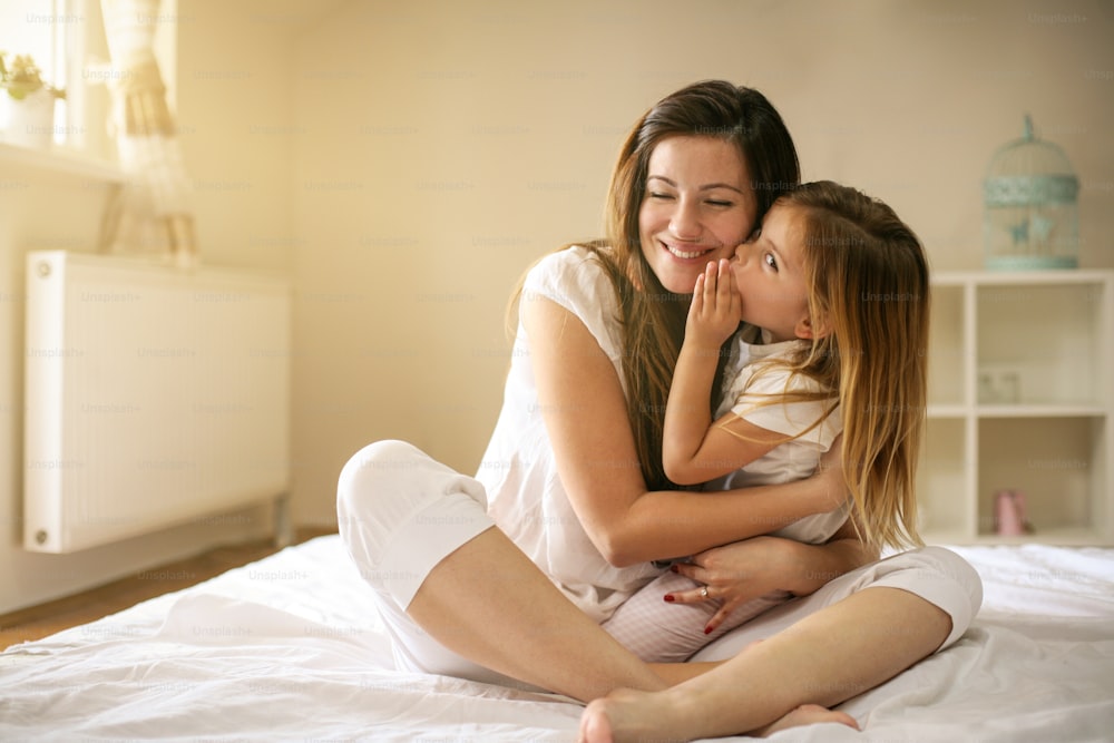 ベッドに横たわるかわいい娘を持つお母さん。「n自由時間に一緒に楽しむ。 母親に秘密をささやく少女。