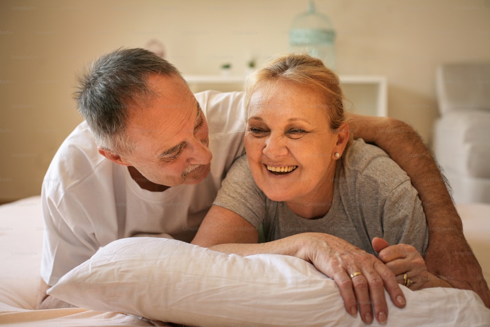 Senior couple lying on bed and having funny conversation. Senor man hugging senior woman.