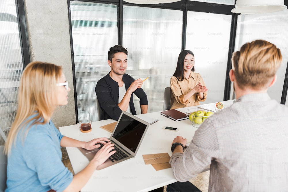 Busy office workers are sitting around table and doing their job together. Concentrated woman is typing on laptop