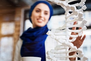 Neue Perspektive. Selektiver Fokus des DNA-Modells mit muslimischer Frau, die es im Hintergrund lernt