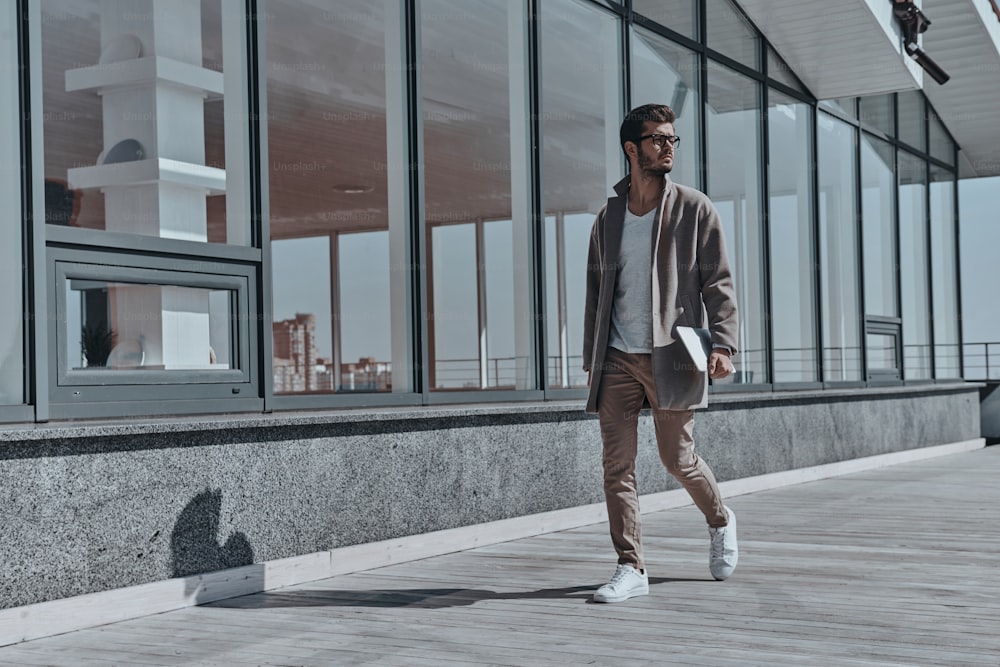 Full length of confident young and handsome man carrying digital tablet while walking outdoors