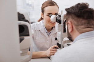 True enthusiast. Cheerful positive beautiful doctor smiling and testing the vision of her patient while enjoying her job