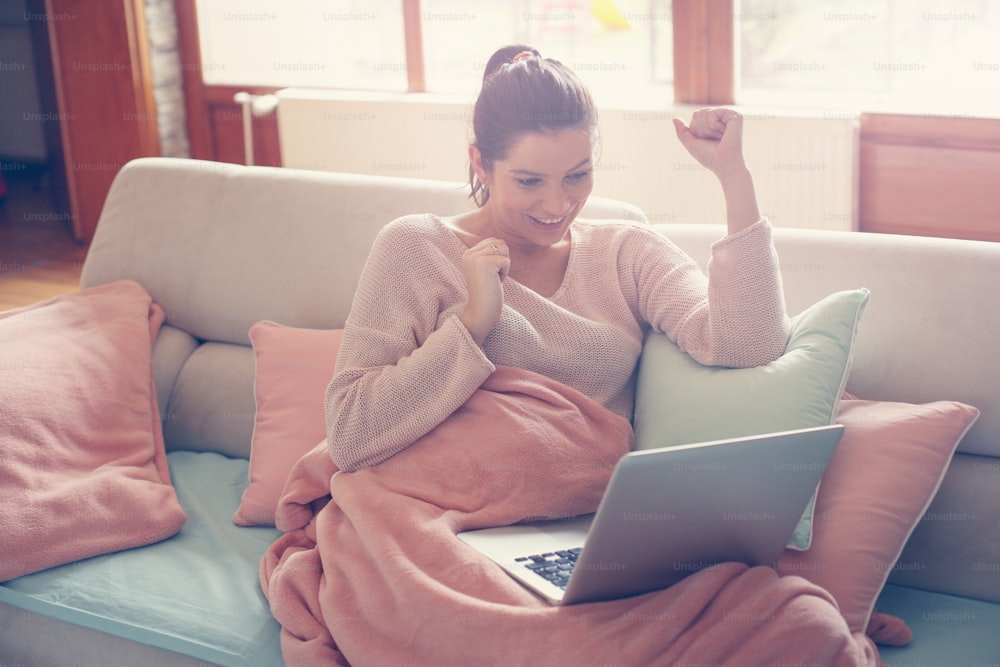 Caucasian pregnant woman working on a laptop and sitting on a couch at her home.
