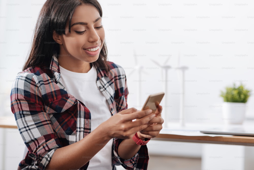 Digital native. Pleasant nice young woman holding her smartphone and typing a message while doing social networking