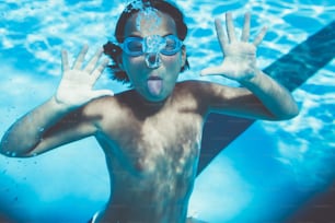 Underwater fun. Cute little girl with goggles swimming underwater and diving in the swimming poll. Sport and leisure.