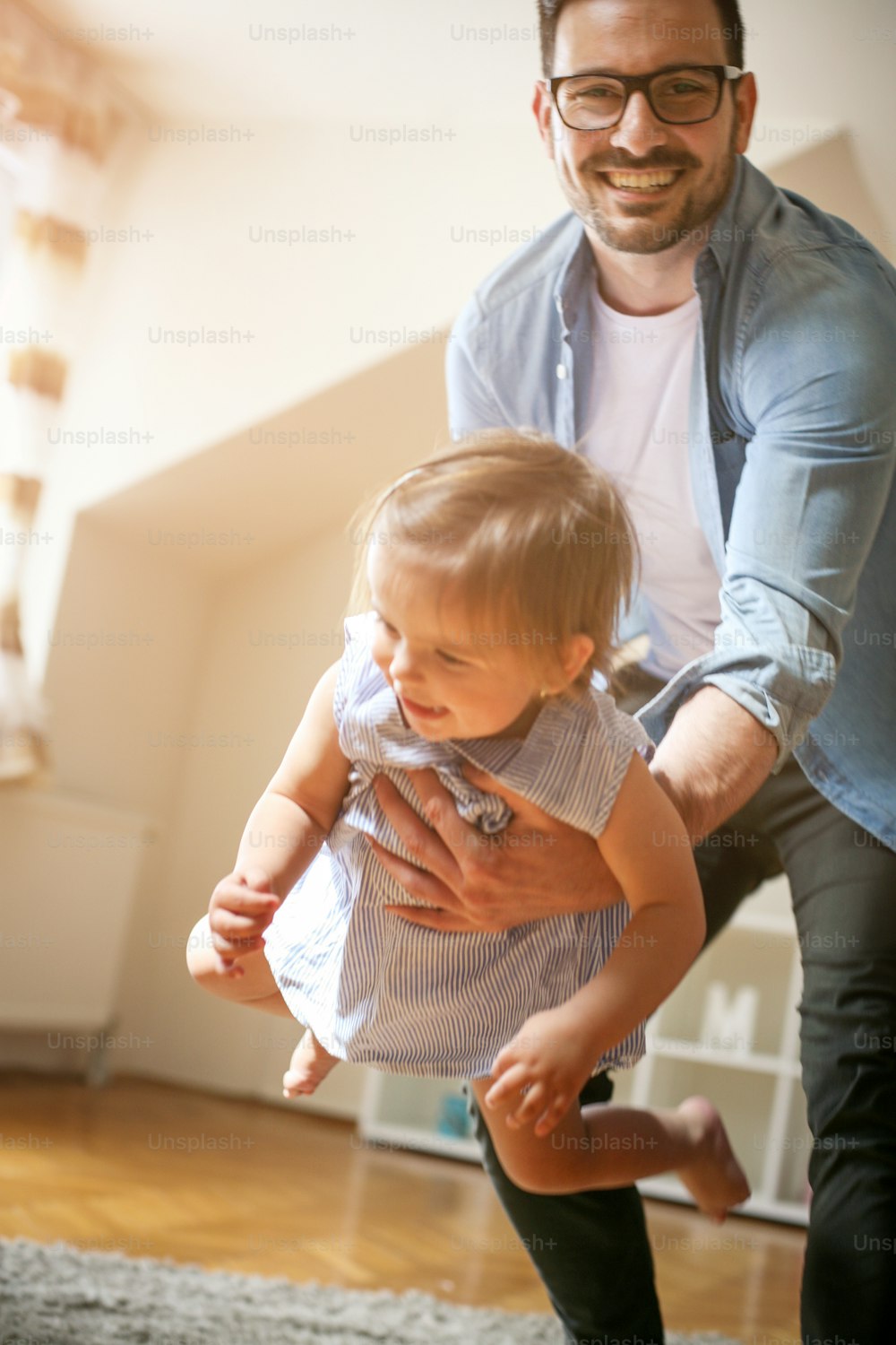Happy father playing with his daughter. Cheerful father holding in hands his little baby and playing with her. Looking at camera.