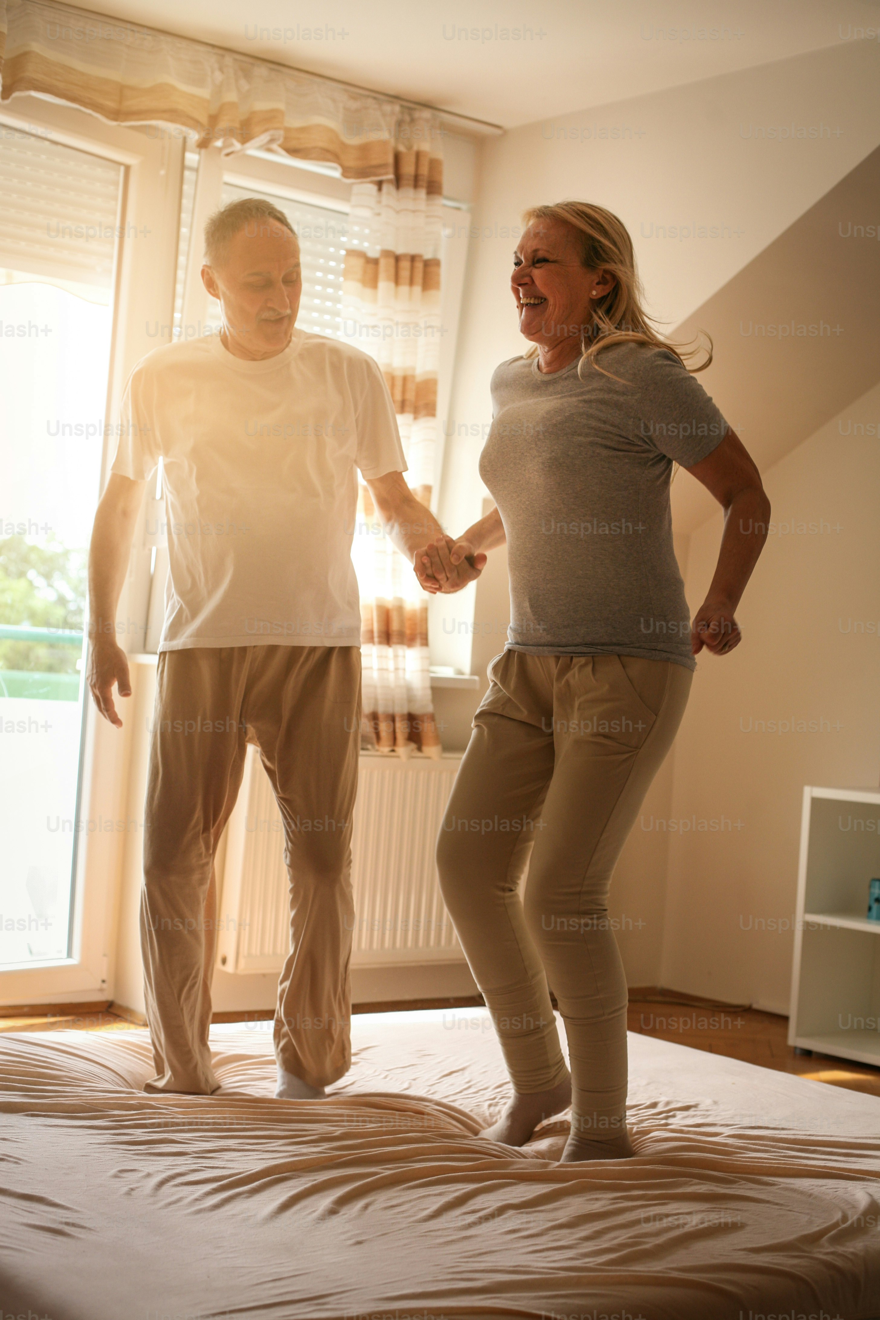 Senior pareja bailando y saltando juntos en la cama tomados de la mano.