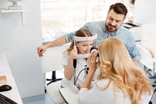 Lovely relationships. Prominent qualified nice ophthalmologist checking girls eyes while her father sitting beside her and supporting her