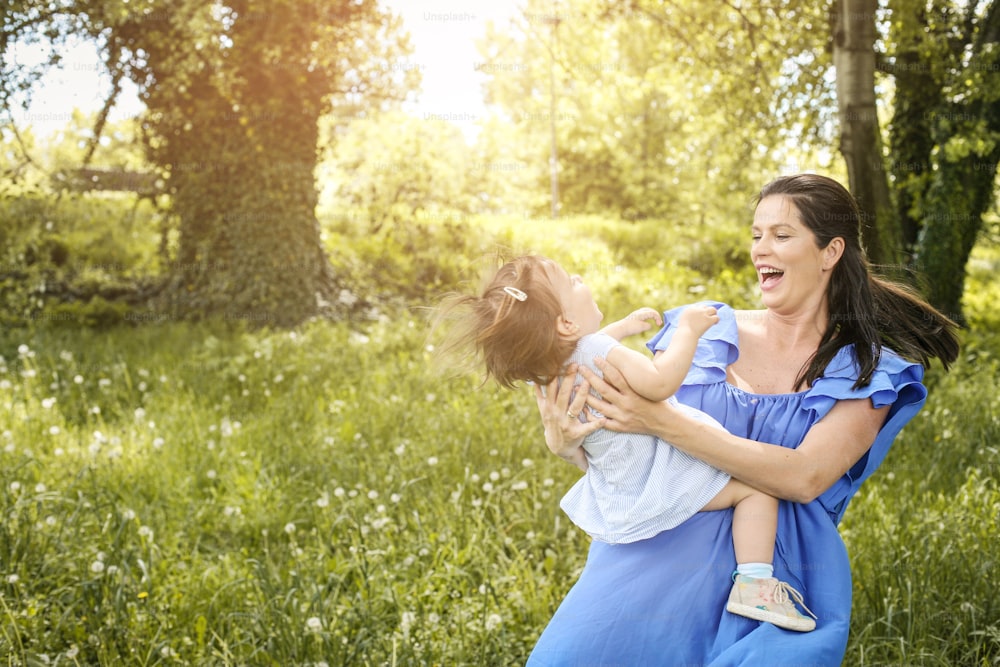 Pregnant mother playing with little daughter in park. Mother and daughter in meadow.