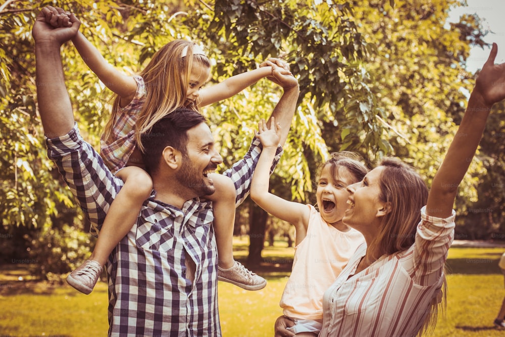 Familia feliz jugando juntos en el prado y disfrutando en el día de verano. Niña sentada sobre los hombros del padre.
