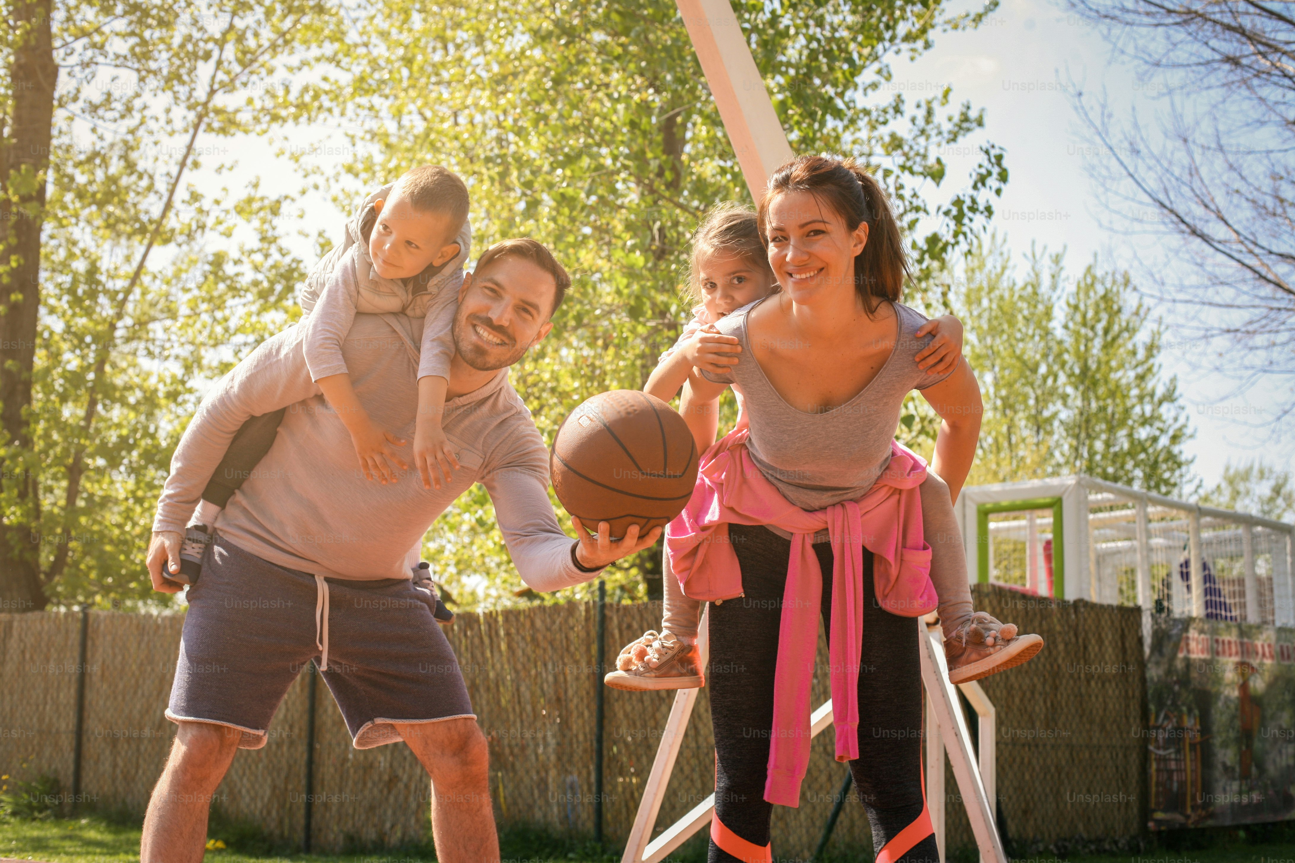 Padres jugando con sus hijos en el parque con baloncesto. Mirando a la cámara.