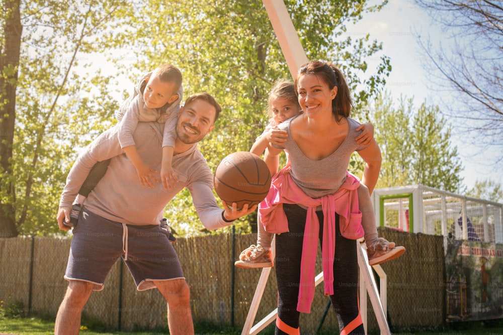 Padres jugando con sus hijos en el parque con baloncesto. Mirando a la cámara.