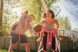 Des parents jouent avec leurs enfants dans le parc avec du basket-ball. Regarder la caméra.