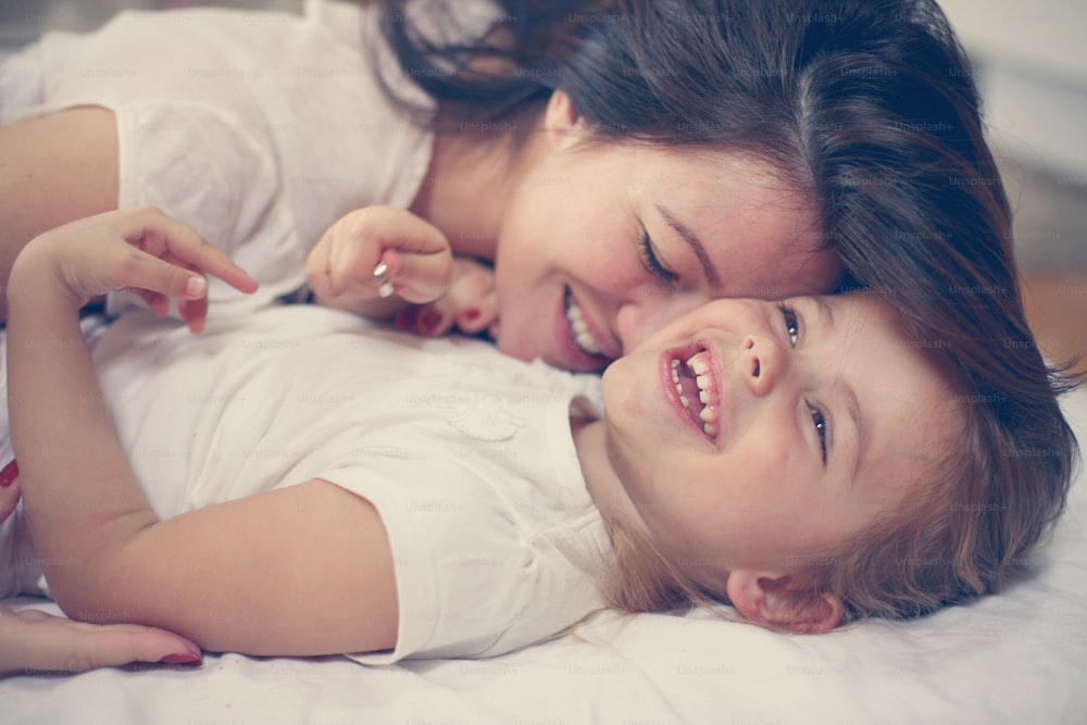 ベッドの上で幼い娘と遊ぶ若い母親。自由時間に一緒にお楽しみください。