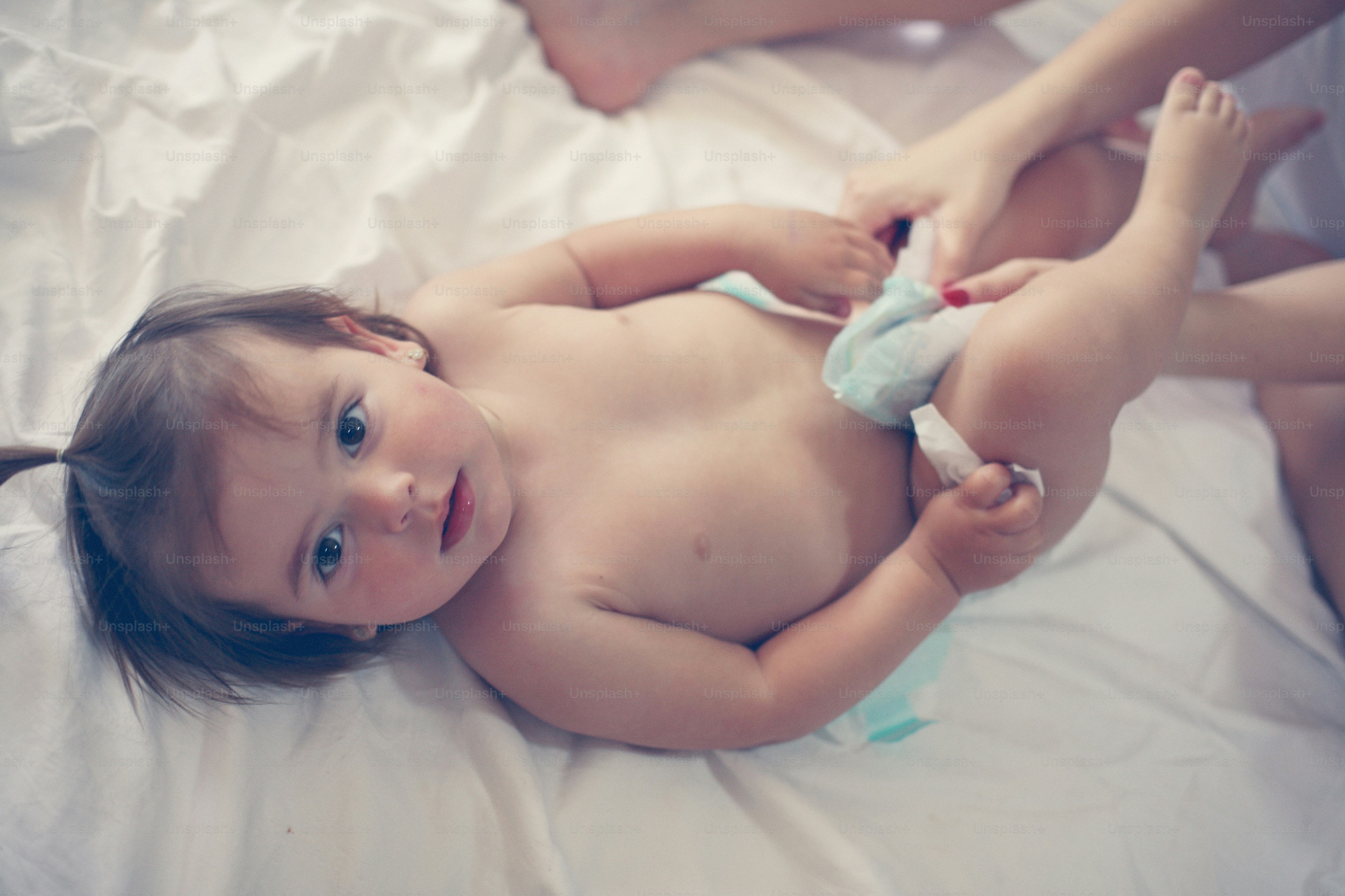 Mother with her baby at home. Mother changing diaper her little baby on the bed. Little baby looking at camera.