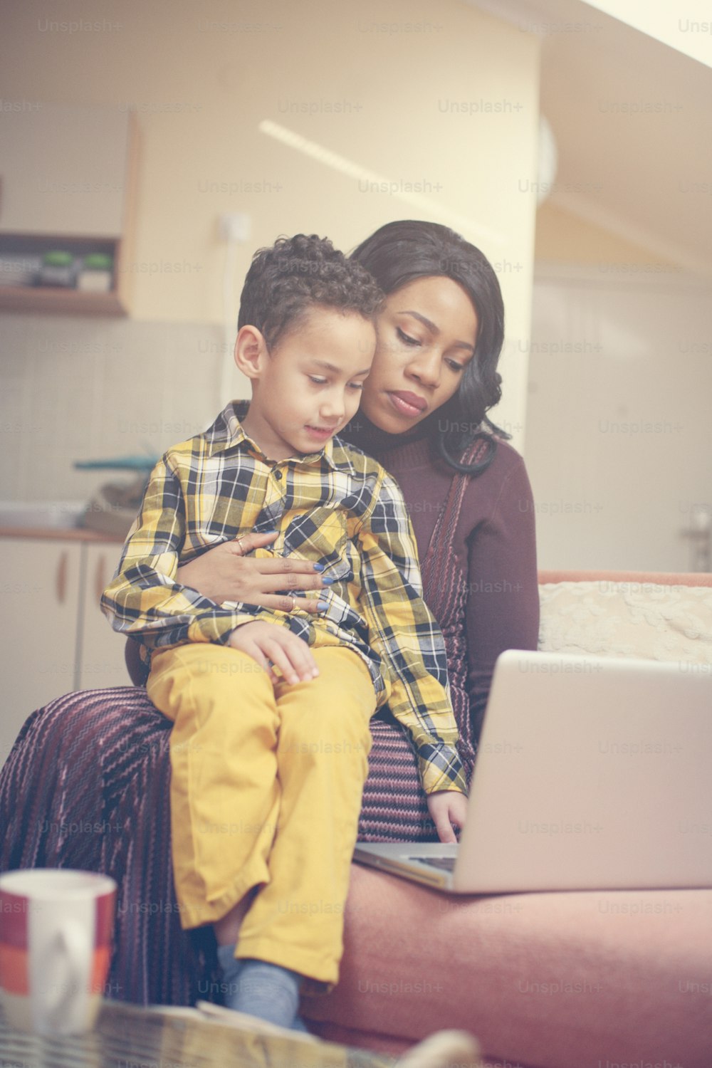 Una mujer afroamericana y su hijo usando una computadora portátil en casa.