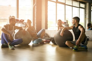 Group of people workout in healthy club. People having conversation after Pilates exercise with Pilates ball.