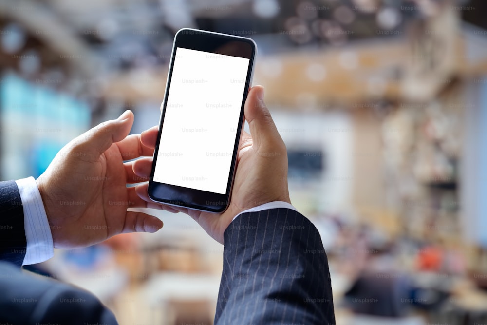 Imagen recortada de un hombre de negocios usando un teléfono inteligente, mirando la pantalla en blanco mientras descansa en un café. Teléfono móvil con pantalla en blanco para montaje gráfico.