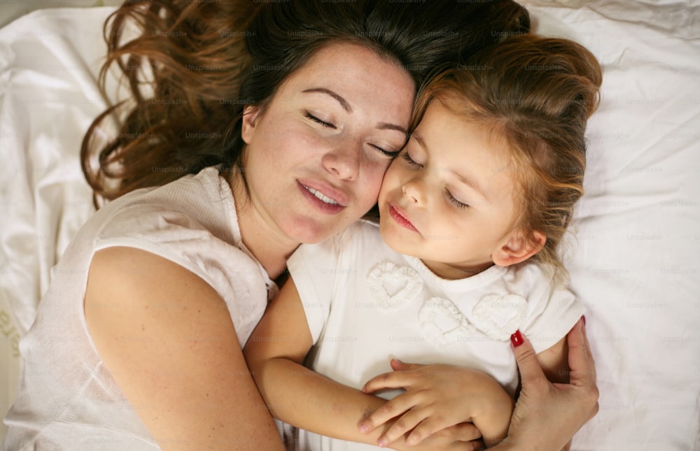 Mother and daughter sleeping together in bed. Mother and daughter embracing in bed asleep.