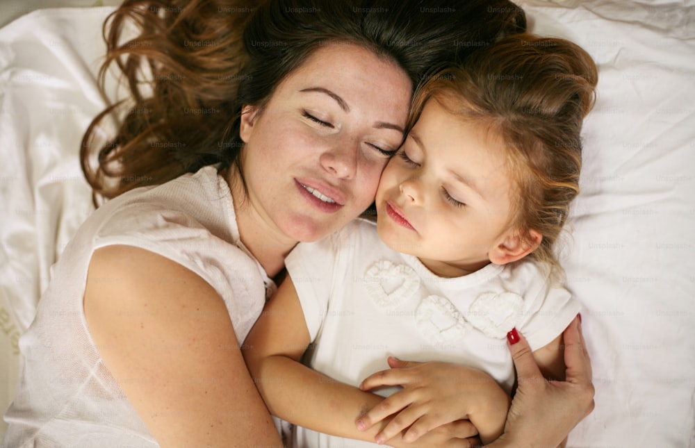 Mother and daughter sleeping together in bed. Mother and daughter embracing in bed asleep.