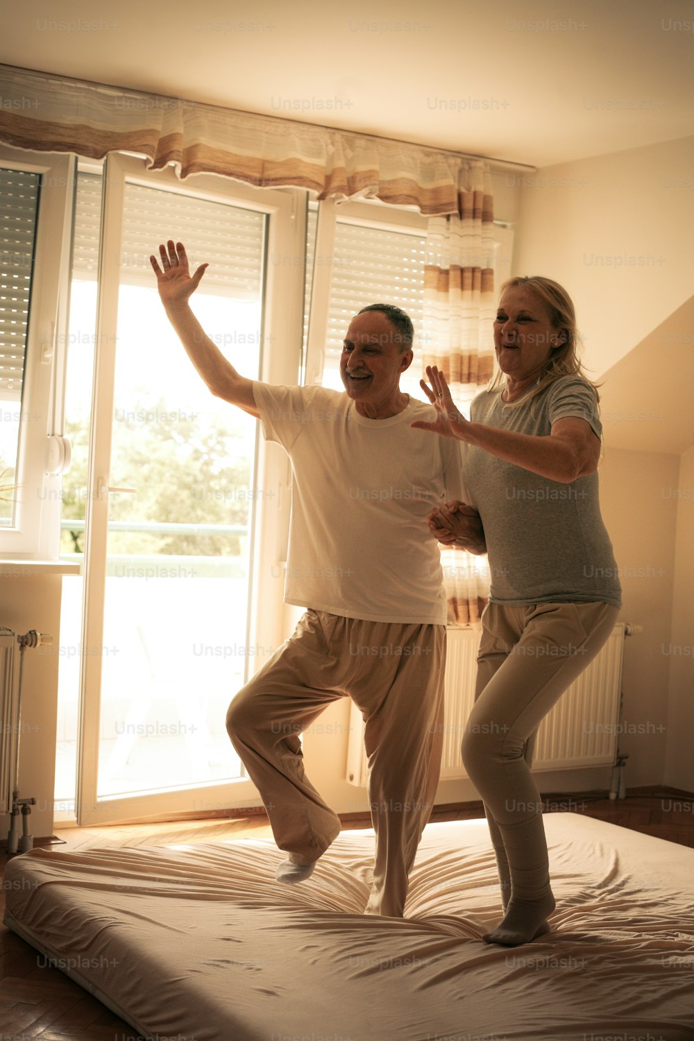 手をつないでベッドの上で一緒に踊ったり飛び跳ねたりする老夫婦。