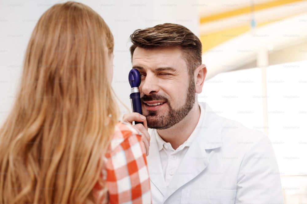 Try not to move your eyes. Prominent capable handsome guy employing professional ophthalmoscope for indicating problems and diagnosing his patient