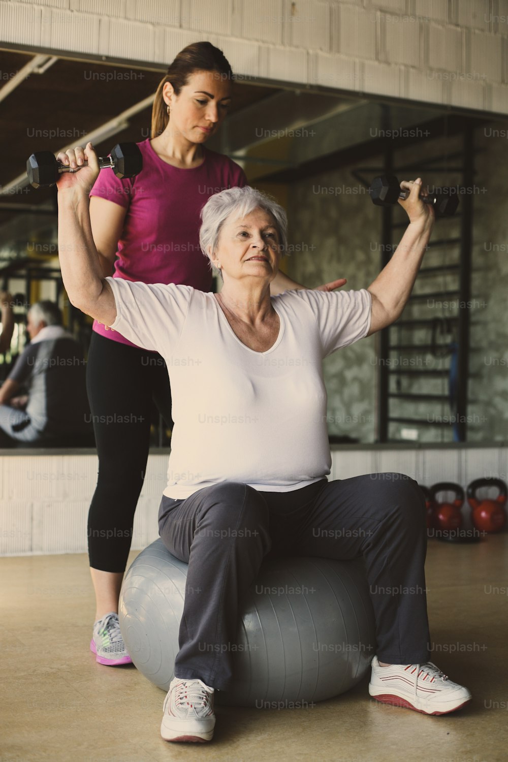リハビリセンターでの高齢女性のトレーニング。先輩女性を助けるパーソナルトレーナー