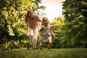 Mother and daughter running trough meadow. Mother chases her daughter.