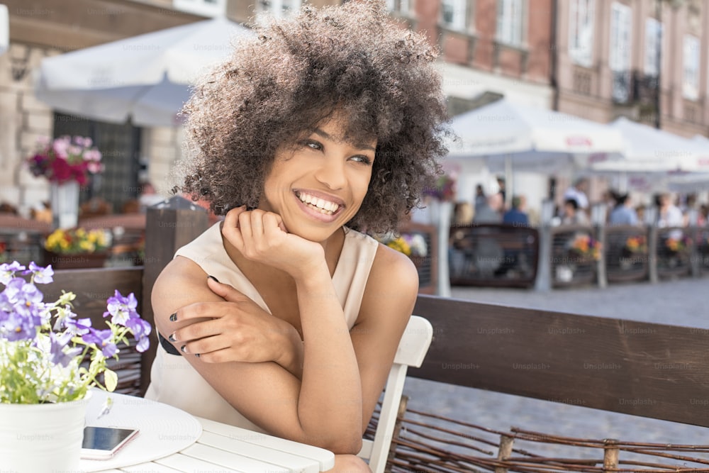 Beautiful young african american woman sitting at cafe, sunny day.