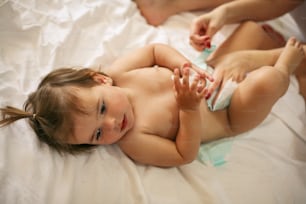 Mother with her baby at home. Mother changing diaper her little baby on the bed.