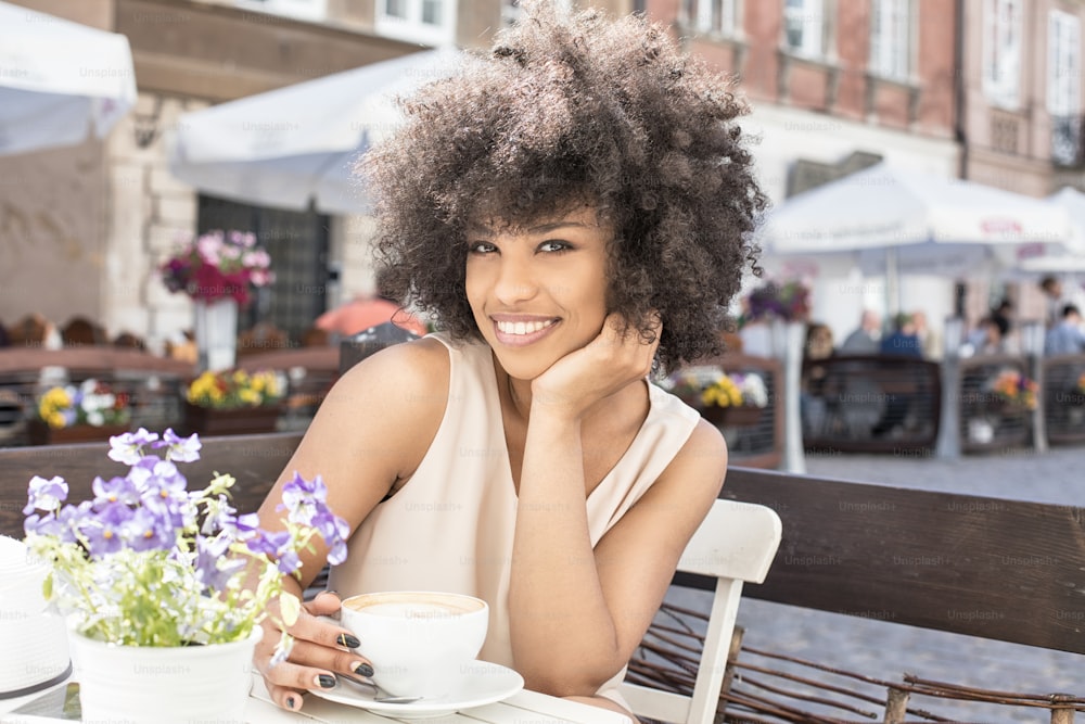 Beautiful young african american woman drinking coffee at cafe, sunny day.