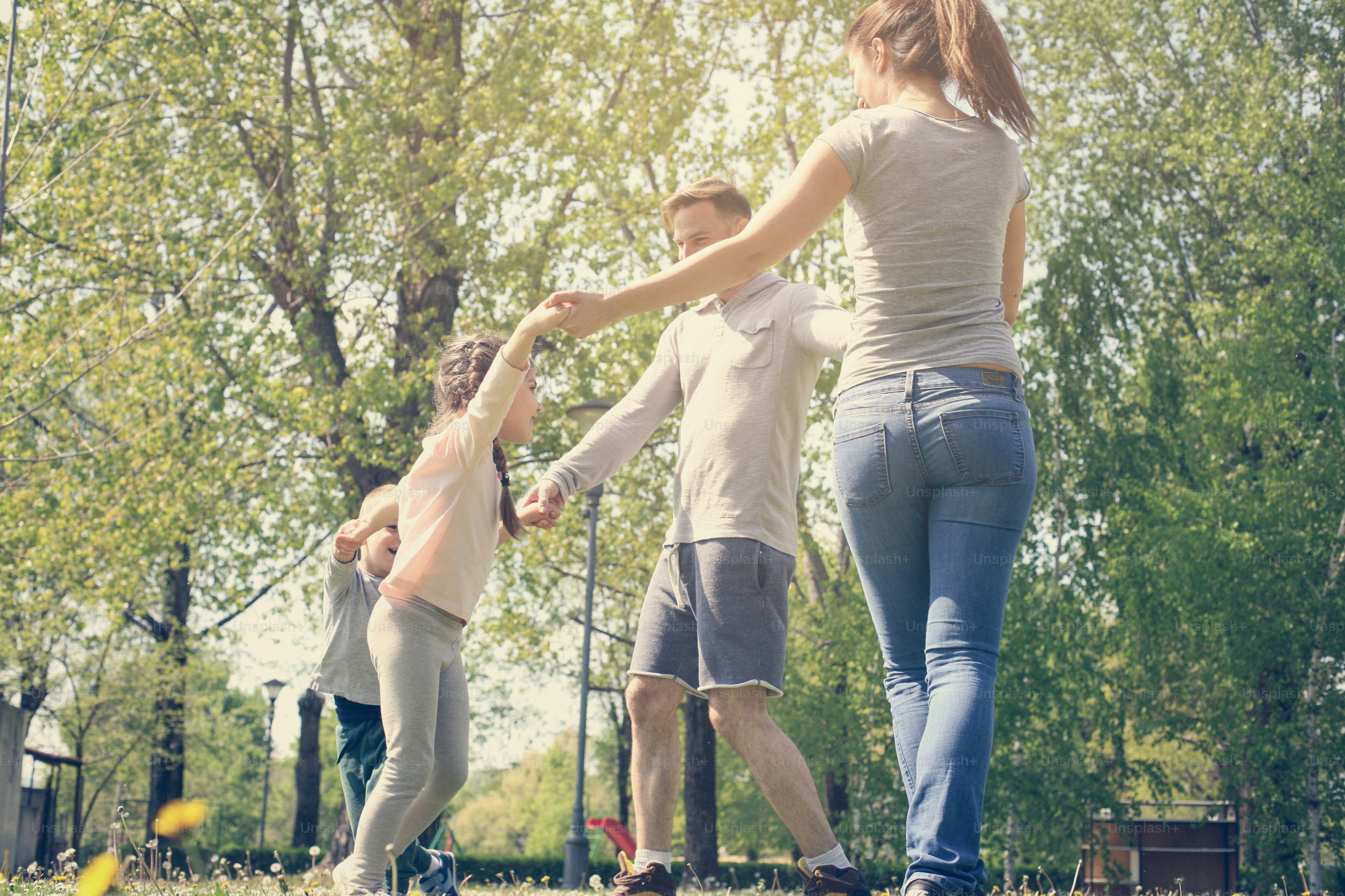 Glückliche Eltern spielen mit ihren Kindern auf der Wiese. Familie auf Wiese Händchen haltend und im Kreis drehend.