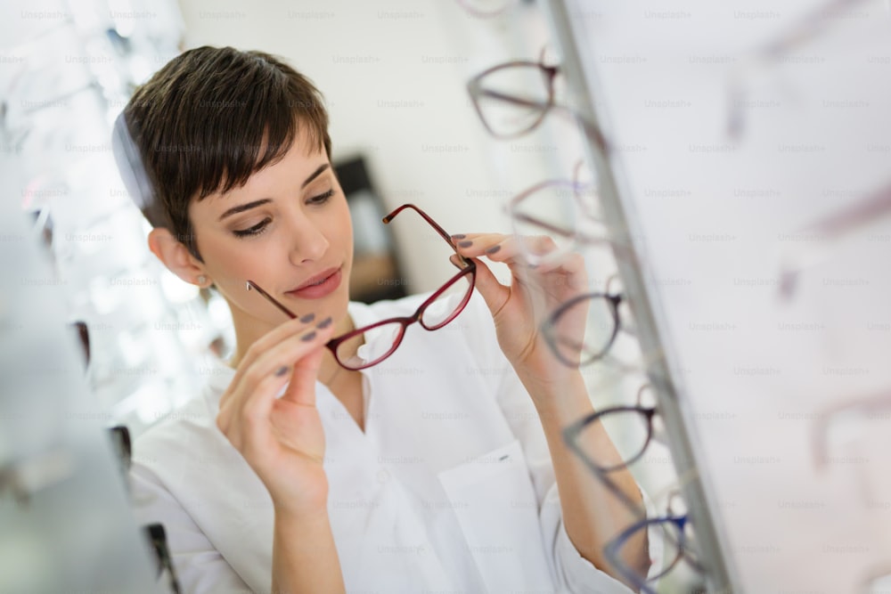 Hübsche junge Frau wählt neue Brille im Optikgeschäft, um das Sehvermögen zu korrigieren