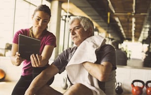 Senior man workout in rehabilitation center. Personal trainer showing something  on digital tablet.