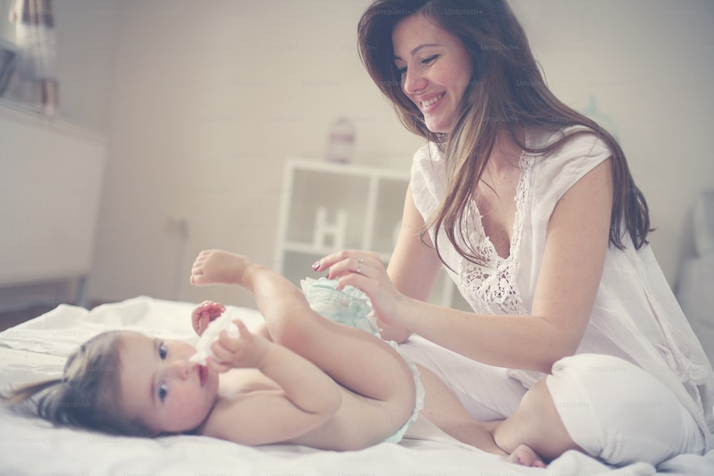 Mother with her baby at home. Mother changing diaper her little baby on the bed.