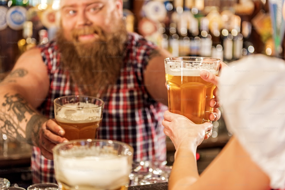 Focus on close up glass of appetizing beer. Female taking it from happy fat bartender in boozer