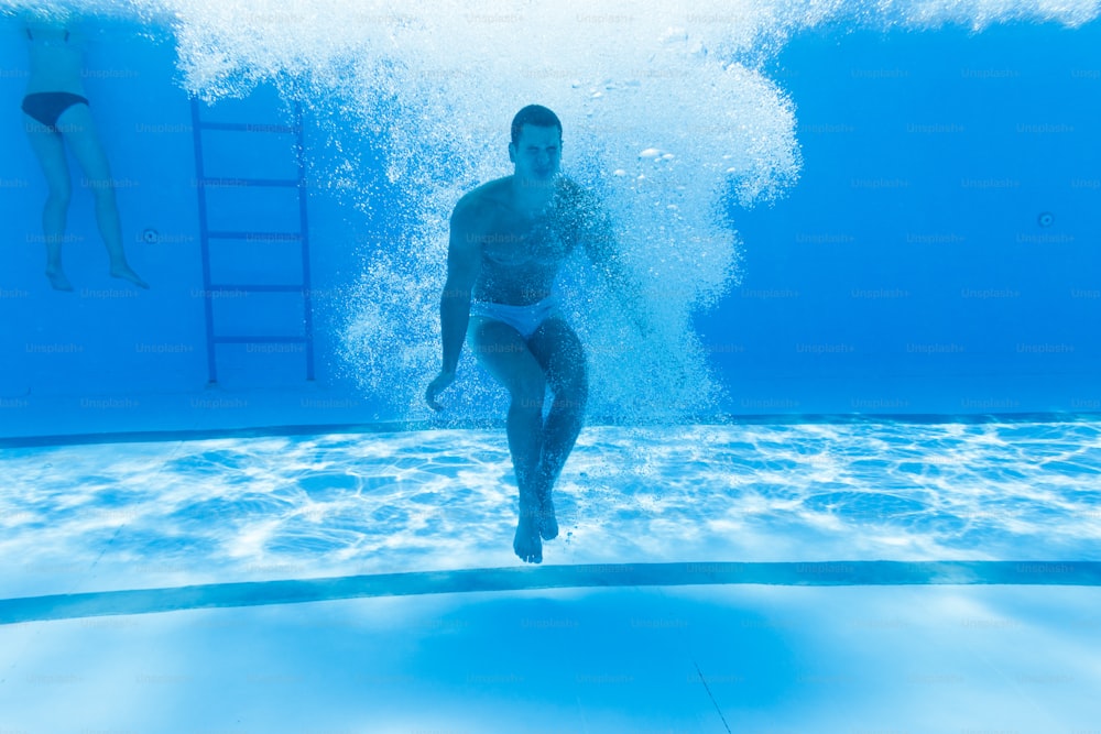 Underwater fun. Young handsome man swimming underwater and diving in the swimming poll. Sport and leisure.