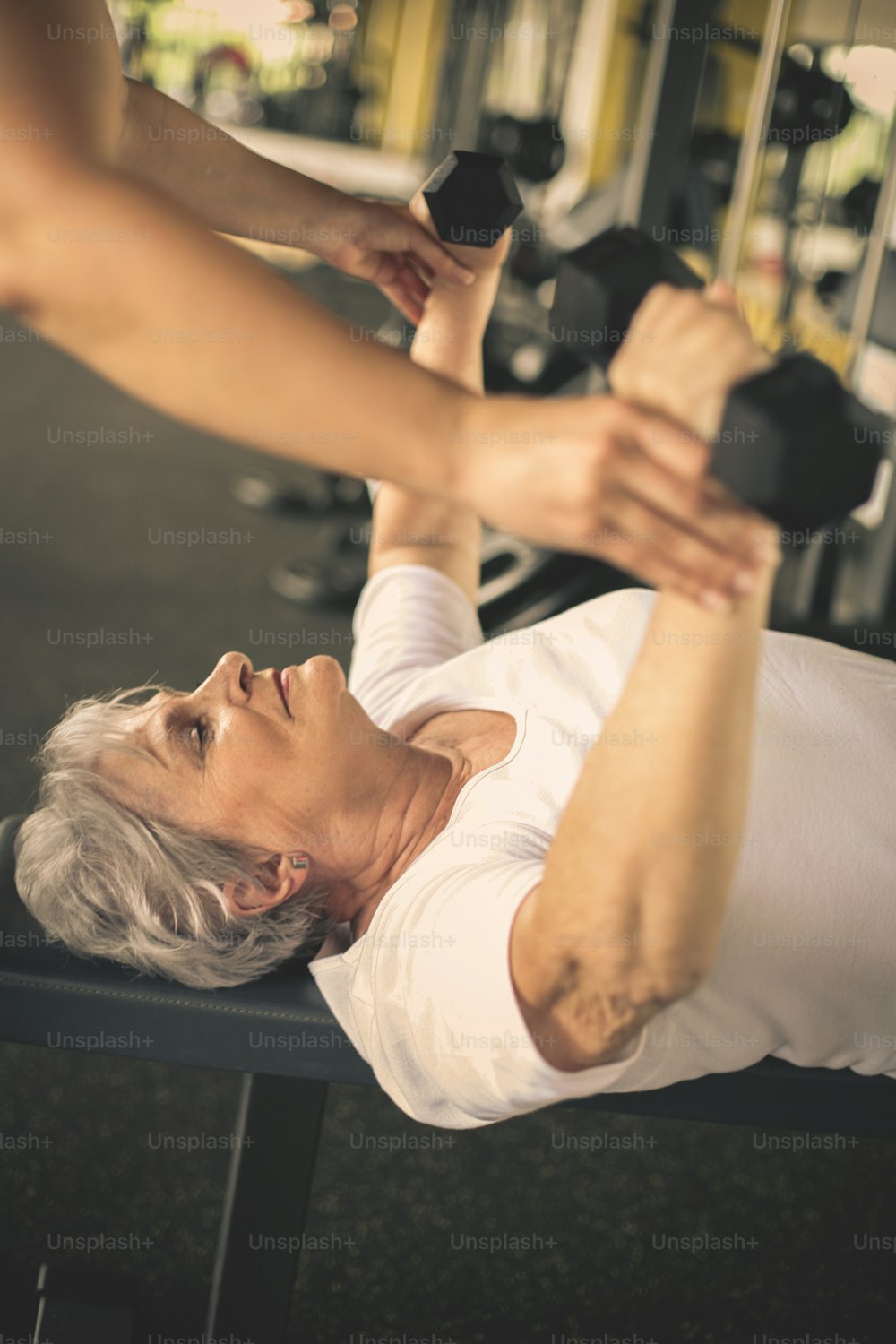 Esercizio di lavoro del personal trainer con la donna anziana in palestra. Donna solleva il peso. Allenamento in palestra.