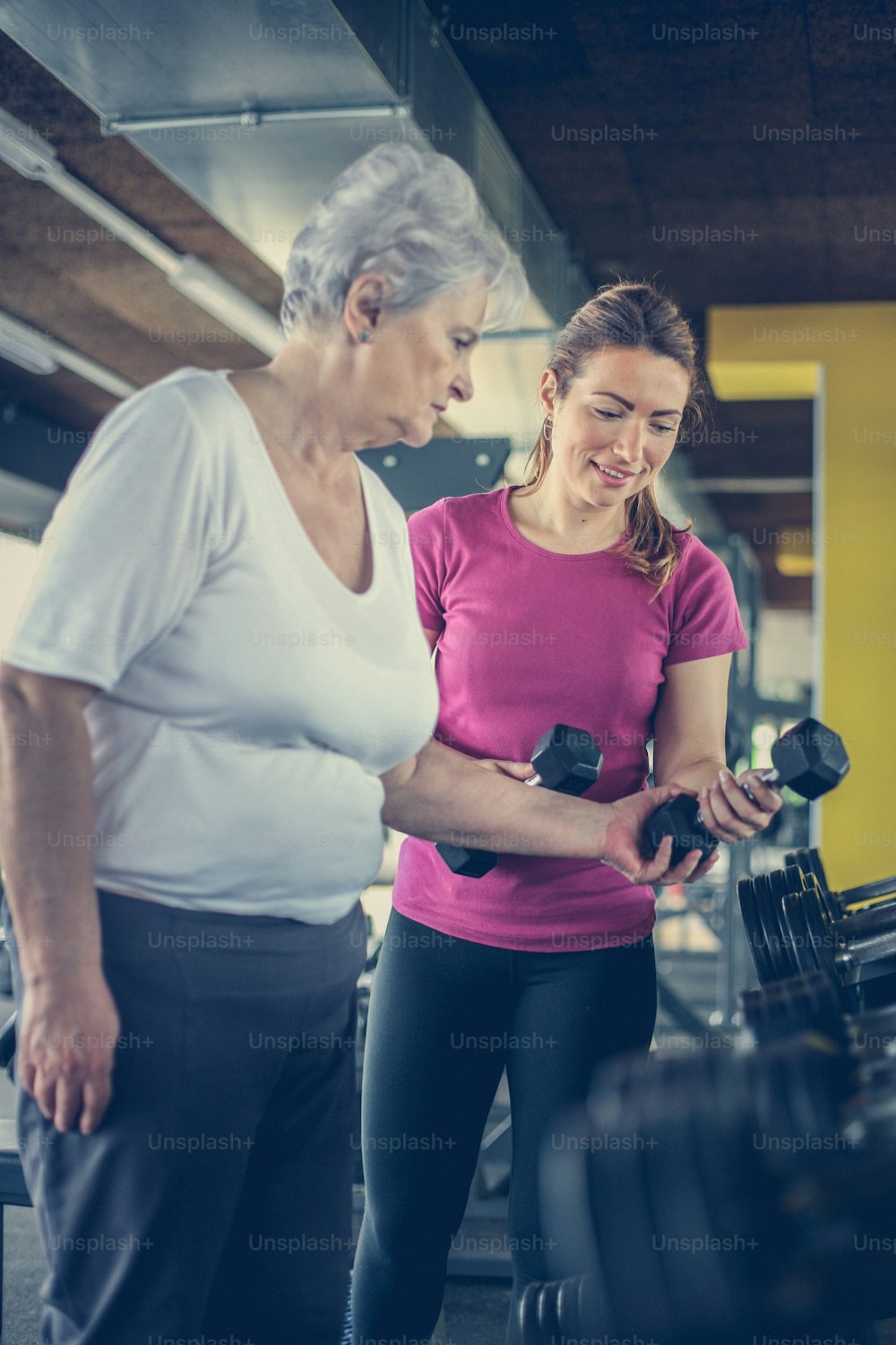 Personal Trainer Arbeitsübung mit älteren Frauen im Fitnessstudio. Frau nimmt Gewicht. Workout im Fitnessstudio