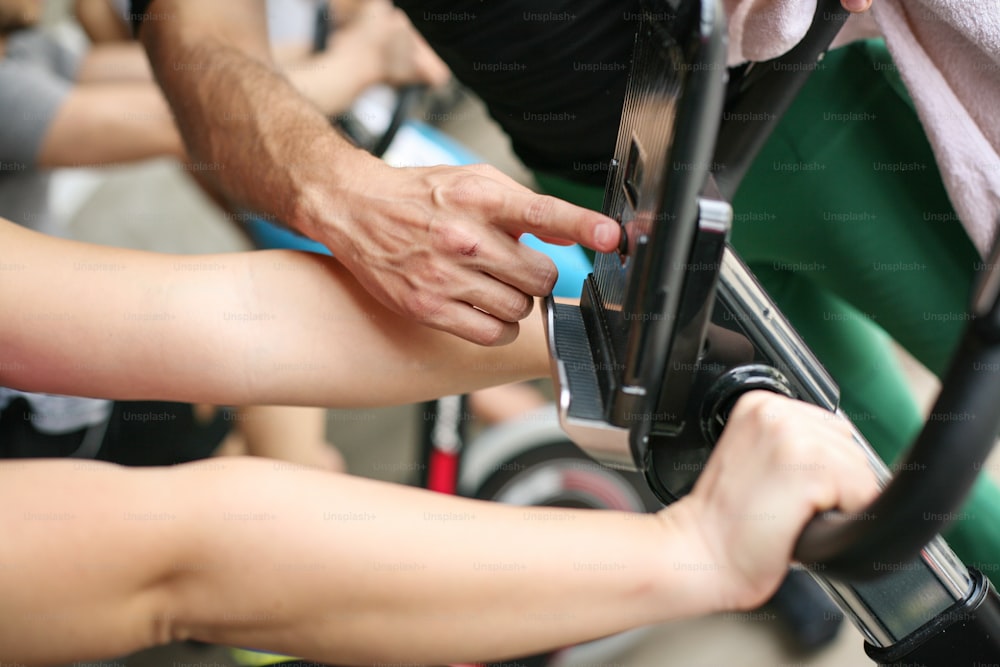 Close up of people hands. Personal trainer changes the speed of the bicycle."n