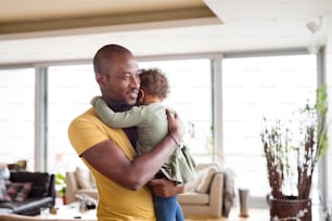 Young afro-american father at home with his cute little daughter holding her in the arms, hugging her.