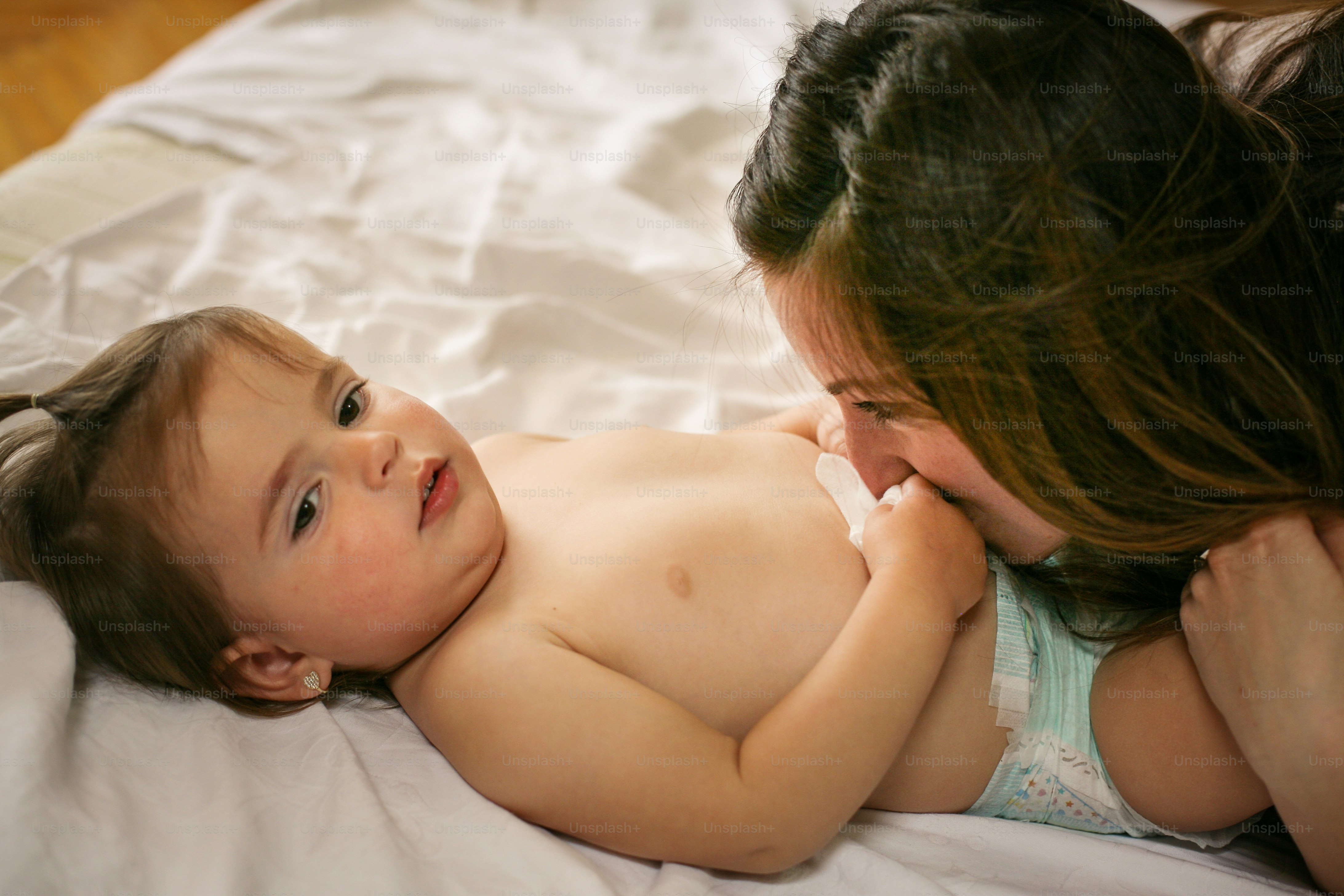 Single mother playing with her little baby at home. Mother and daughter on bed spending time. Mother kissing her baby.
