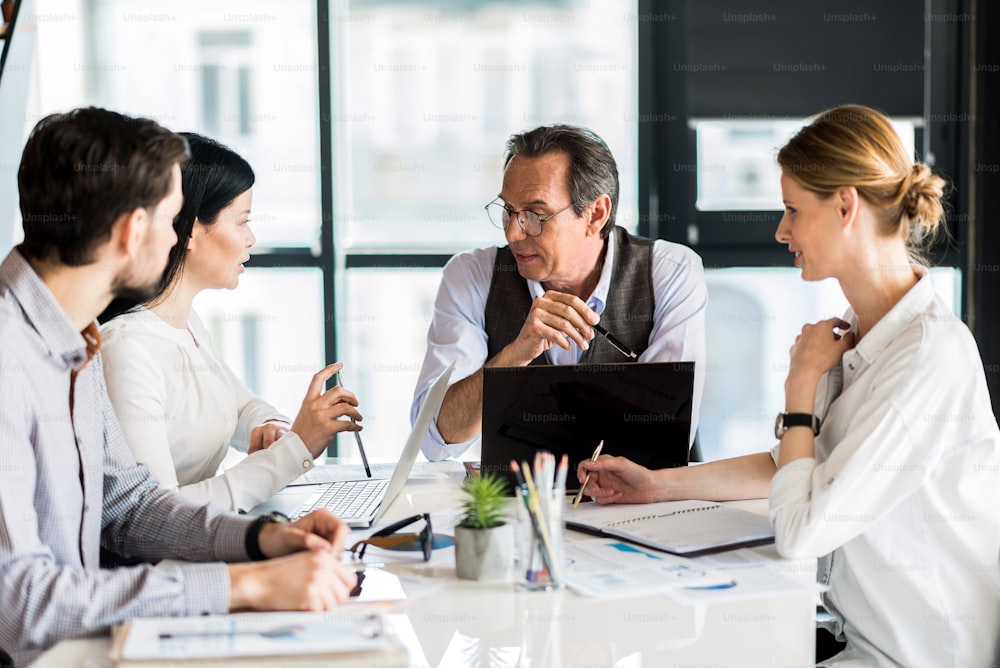 Pleasant work. Involved serious colleagues sitting at table while communicating together. Selective focus on pleasant mature man keeping pencil thoughtfully