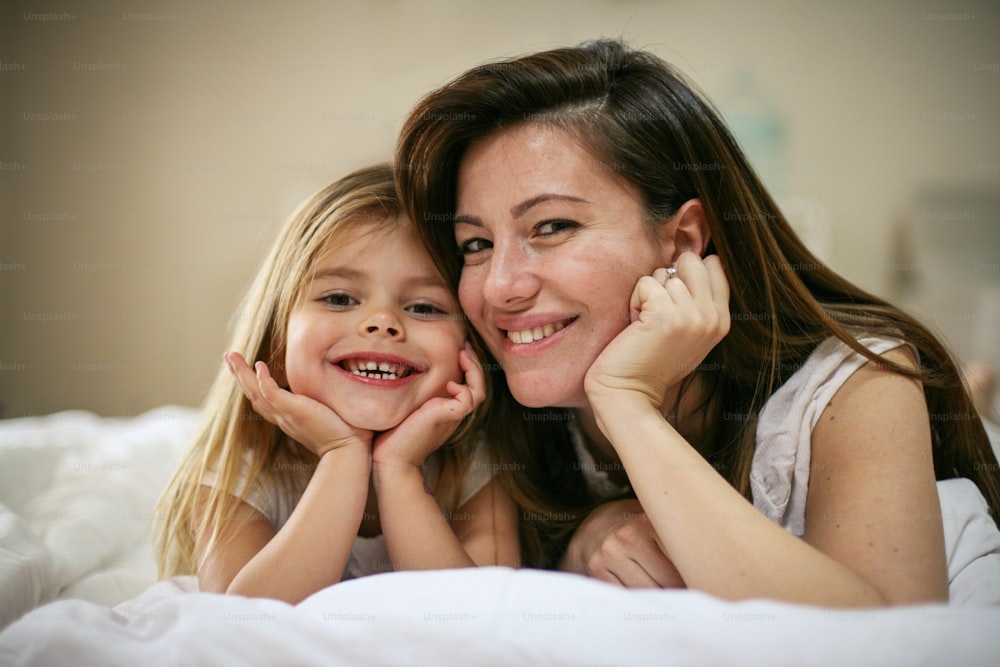 Mother with her cute little daughter lying on bed. "nEnjoy together in free time. Looking at camera.