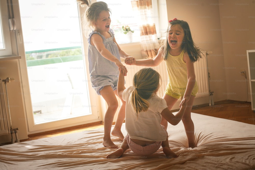 어린 소녀들이 침대에서 함께 즐거운 시간을 보내고 있습니다. 어린 소녀들은 침대에서 집에서 놀고 있습니다.