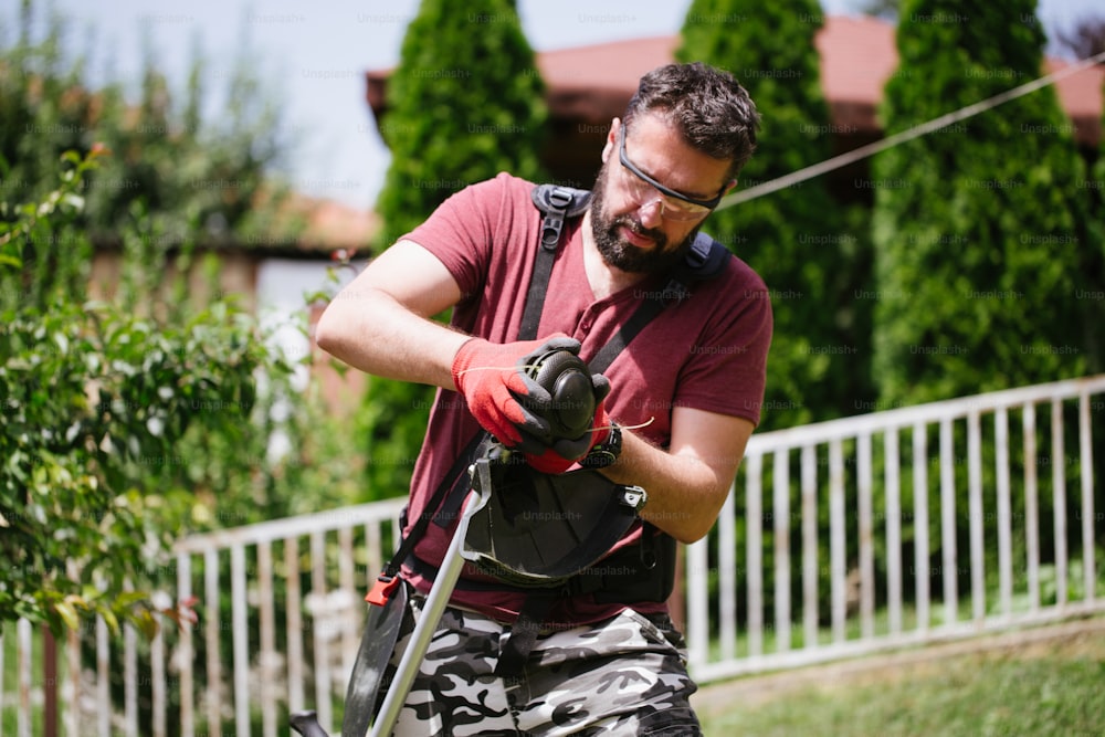 Middle aged man with beard working with grass trimmer in home yard or garden