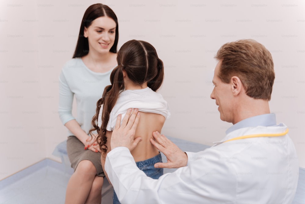Rückenhaltung. Netter kompetenter regelmäßiger Arzt, der eine Untersuchung der Wirbelsäule von Mädchen durchführt und nach einer Ursache für Skoliose sucht